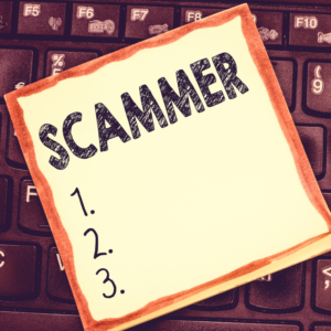 a post it note on a keyboard with "Scammer" written on it